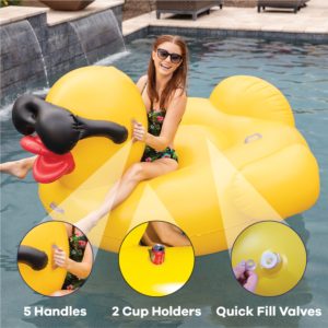 Woman smiling while sitting and floating on a giant yellow rubber ducky with black sunglasses pool float while floating in a pool